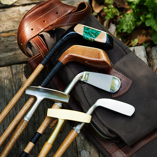 Four handmade hickory golf clubs resting on a vintage golf bag