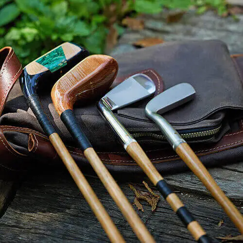 Four handmade hickory golf clubs resting on a vintage golf bag